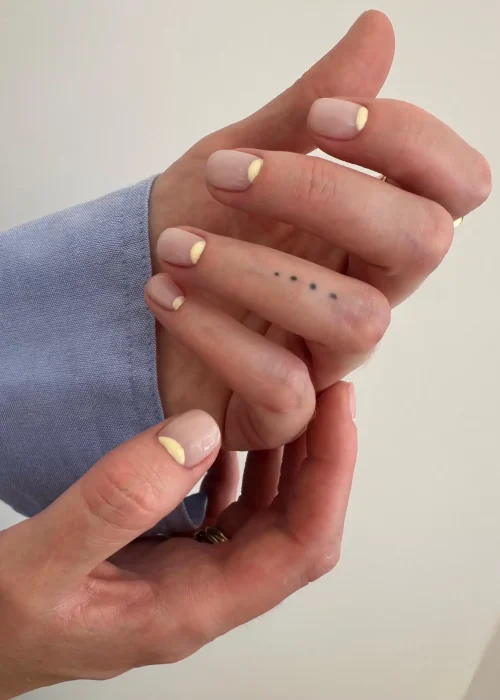 Diseño de Uñas Nude con Media Luna Amarilla Manos mostrando uñas cortas con esmalte nude y diseño de media luna amarillo pastel en la base.