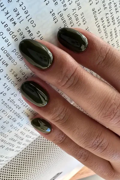 Manicura Verde Militar Oscuro Brillante Mano con uñas largas ovaladas pintadas de color verde militar oscuro brillante sobre un libro